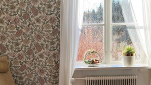 Et værelse med blomstret tapet, en radiator, et vindue med en kurv med frugt og en potteplante.
