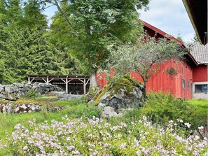 A red barn with a wooden structure nearby, surrounded by greenery and flowers.
