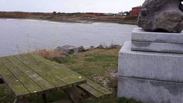 A stone monument with a carved head, a wooden picnic table, and a body of water in the background.