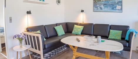 A modern living room with a curved black sofa, a round coffee table, and a painting of a coastal scene.
