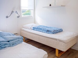 A single bed with a white mattress and a blue blanket, a bedside table with a lamp, and a window with blinds. - 6 Person Holiday Home in Vestervig (Vestervig)
