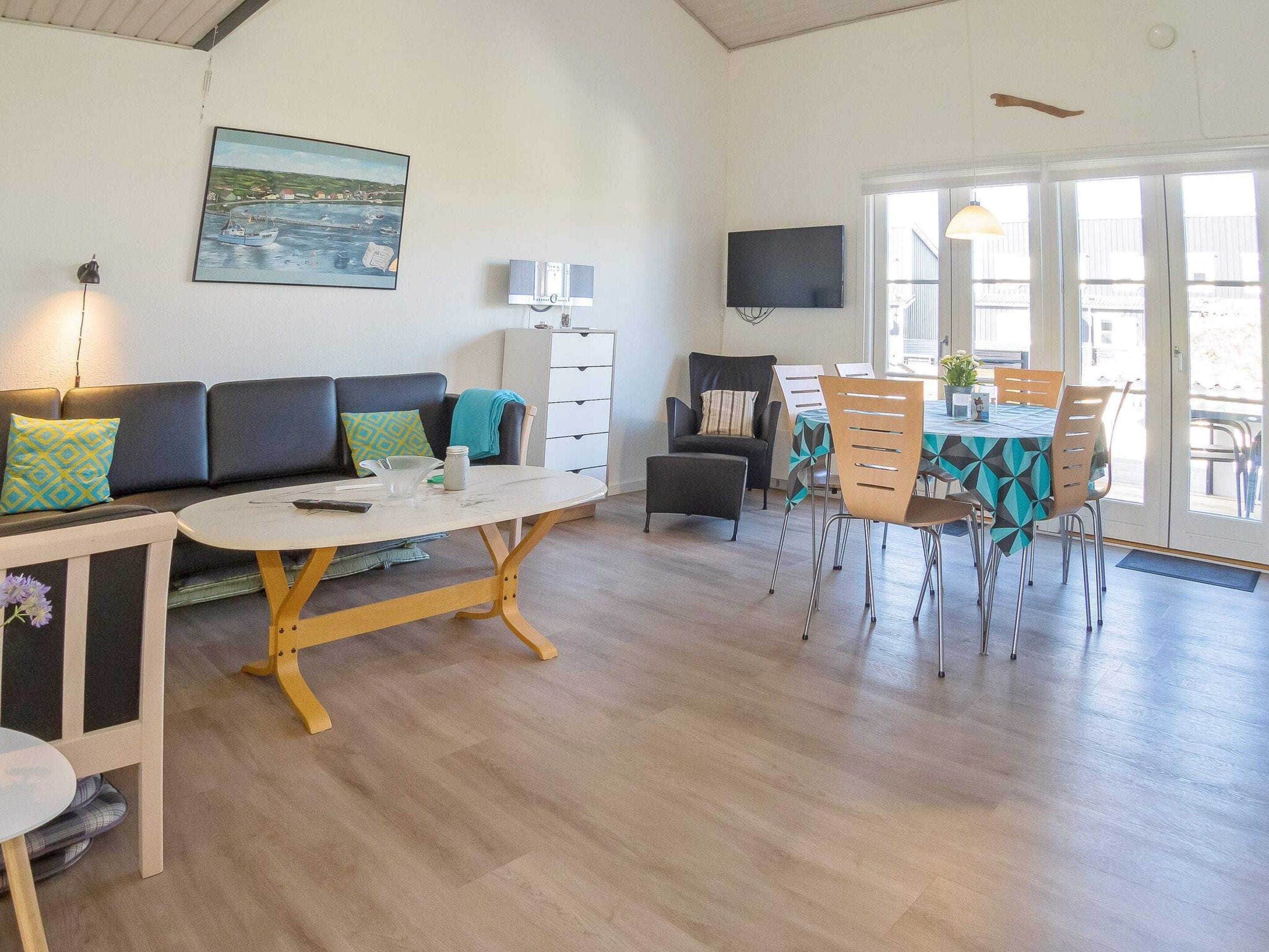 A modern living space with a sofa, dining table, chairs, and a television.