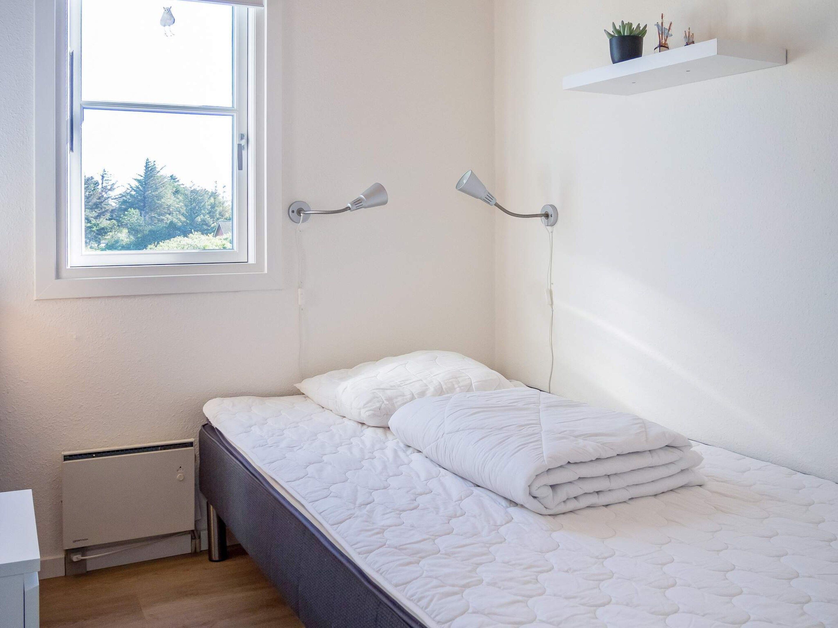 Un dormitorio con cama, ventana, radiador y una estantería en la pared con una planta.