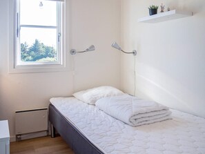 A bedroom with a bed, a window, a radiator, and a wall-mounted shelf with a plant. - 6 Person Holiday Home in Vestervig (Vestervig)