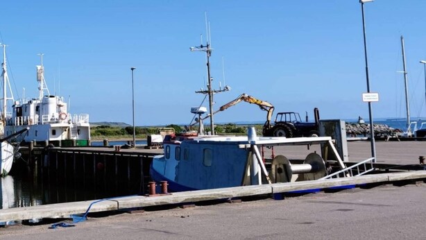 Uma marina com barcos atracados, uma guindaste e céu claro.