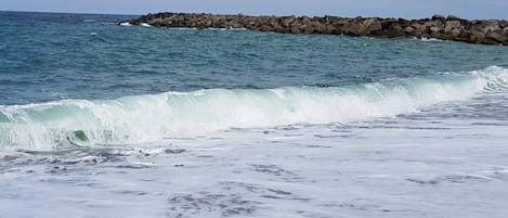A beach with waves crashing onto the shore and a rocky breakwater in the background.