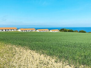 A row of white buildings with orange roofs, likely a hotel, set against a backdrop of a green field and the ocean. - 4 Person Holiday Home in Allinge (Allinge)