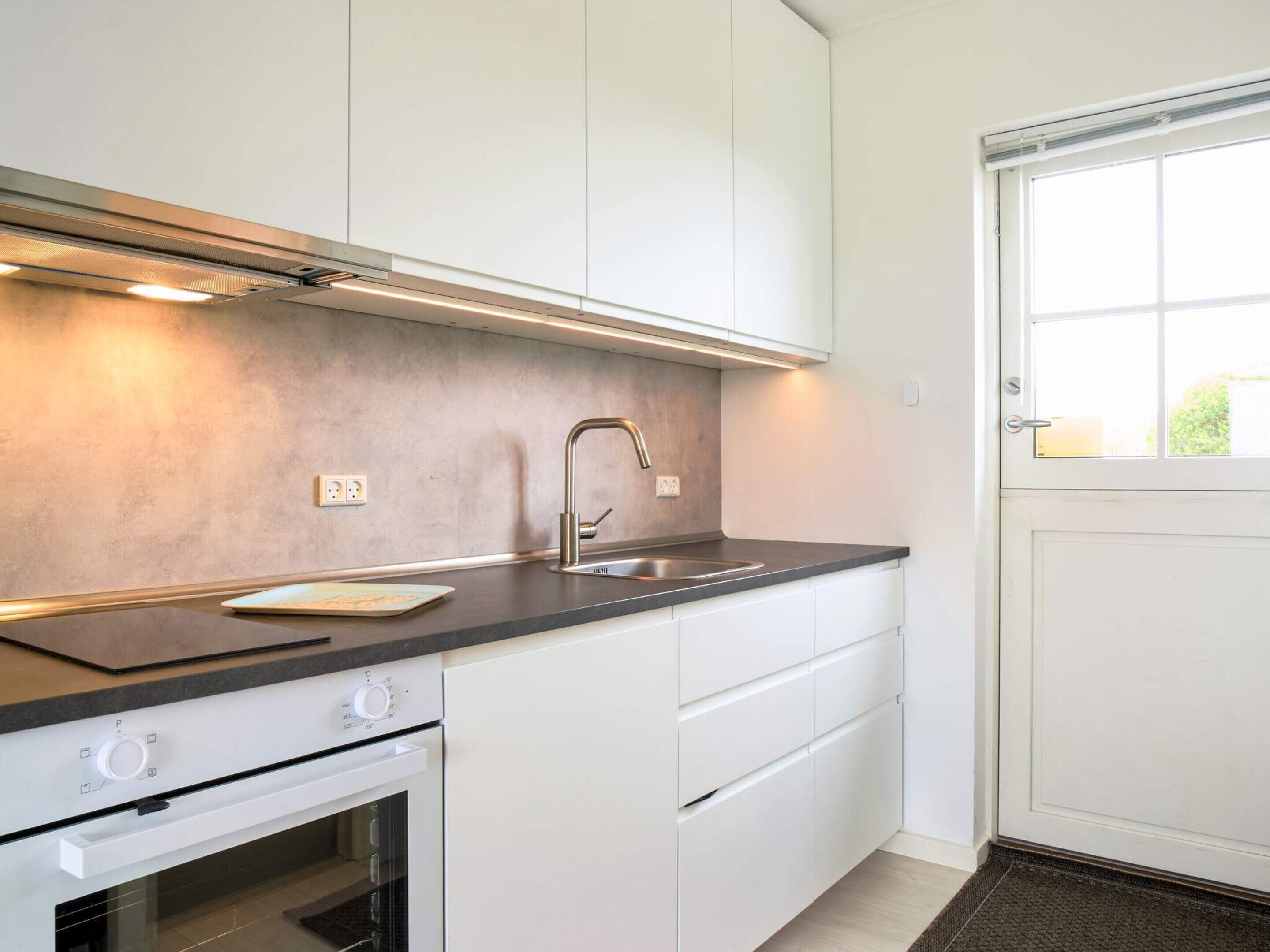 A modern kitchen with white cabinets, a stainless steel sink, and a built-in oven.