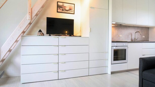 Une cuisine moderne avec des meubles blancs, un four encastré et un coin repas agrémenté d’une chaise noire.