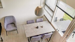 Un coin repas avec une table de couleur claire et quatre chaises, un luminaire suspendu et une vue sur un jardin grâce à de grandes fenêtres.