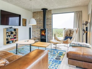 A modern living room with a fireplace, leather furniture, a round table, and a bookshelf. - 5 Star Holiday Home in Lokken (Lokken)