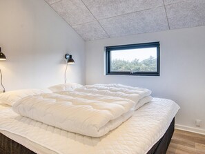 A bedroom with a large bed, a wall-mounted lamp, and a window with a view of trees.