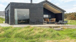 A modern house with a large glass door, a patio with outdoor furniture, and a chimney. - 5 Star Holiday Home in Lokken (Lokken)