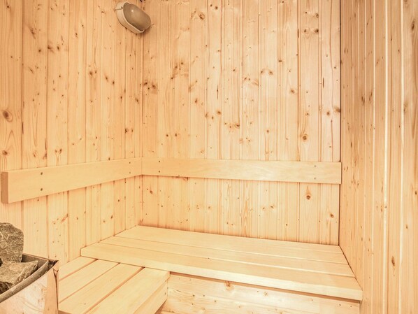 A wooden sauna with benches and a stone seating area.