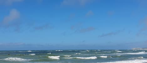 Una playa con olas, cielo despejado y un paseo marítimo de madera.