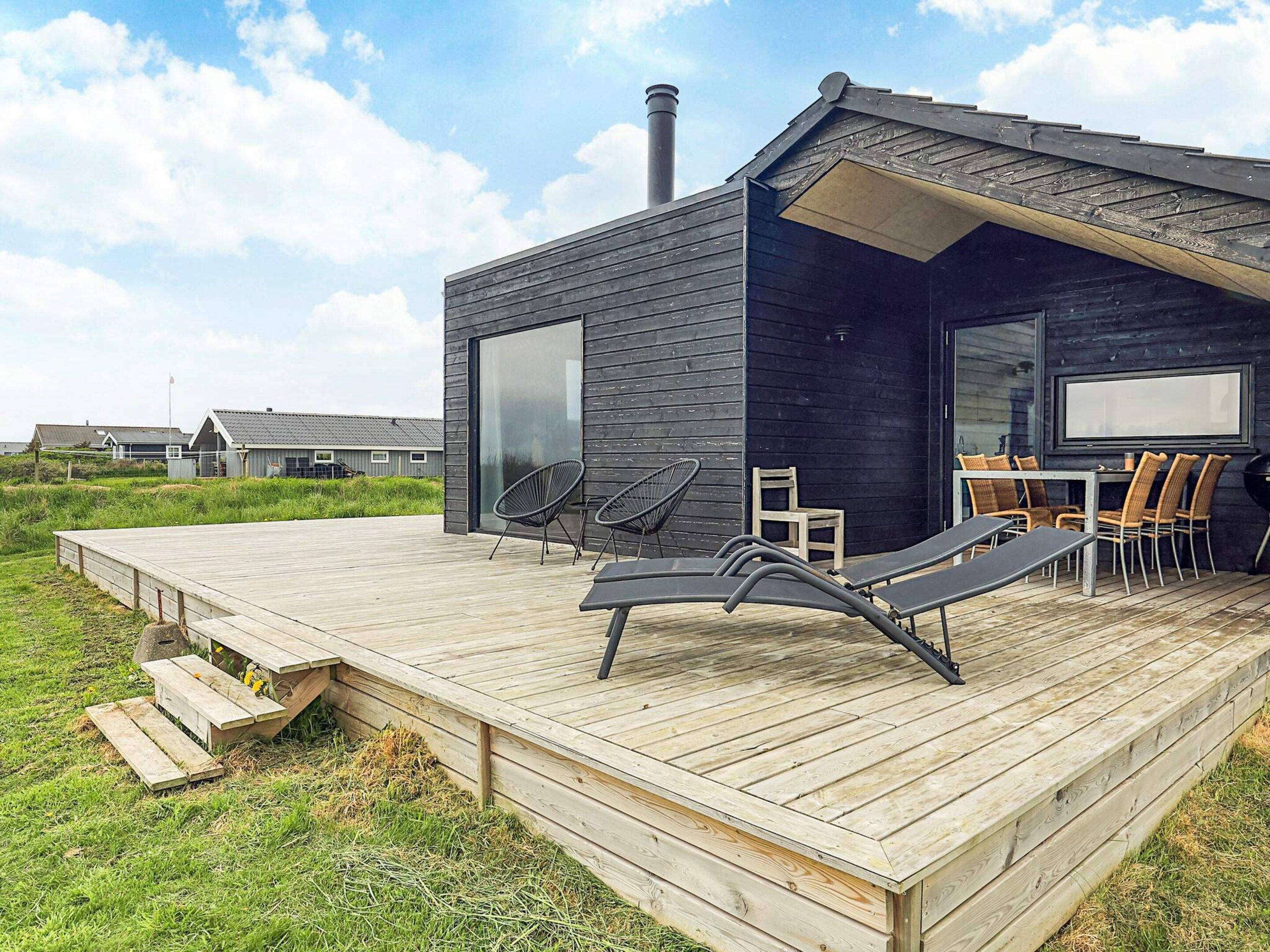 A modern outdoor deck with lounge chairs and a table, surrounded by a wooden deck and grassy area.