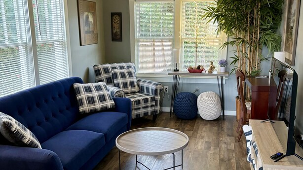 A living room with a blue sofa, a round coffee table, and a wooden dining table. - Jubilee Cottage in the heart of Daphne! (Daphne)