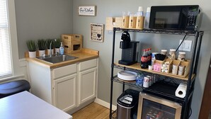 A compact kitchen with a sink, a coffee maker, and a microwave. There are potted plants on the counter, and a shelf with various kitchen items. - Jubilee Cottage in the heart of Daphne! (Daphne)
