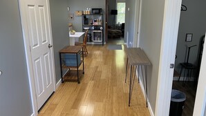 A hallway with a wooden floor, a dining table with chairs, a kitchen area with appliances, and a trash can. - Jubilee Cottage in the heart of Daphne! (Daphne)
