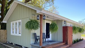 A single-story building with a front porch, two black chairs, a wooden bench, and hanging planters. - Jubilee Cottage in the heart of Daphne! (Daphne)