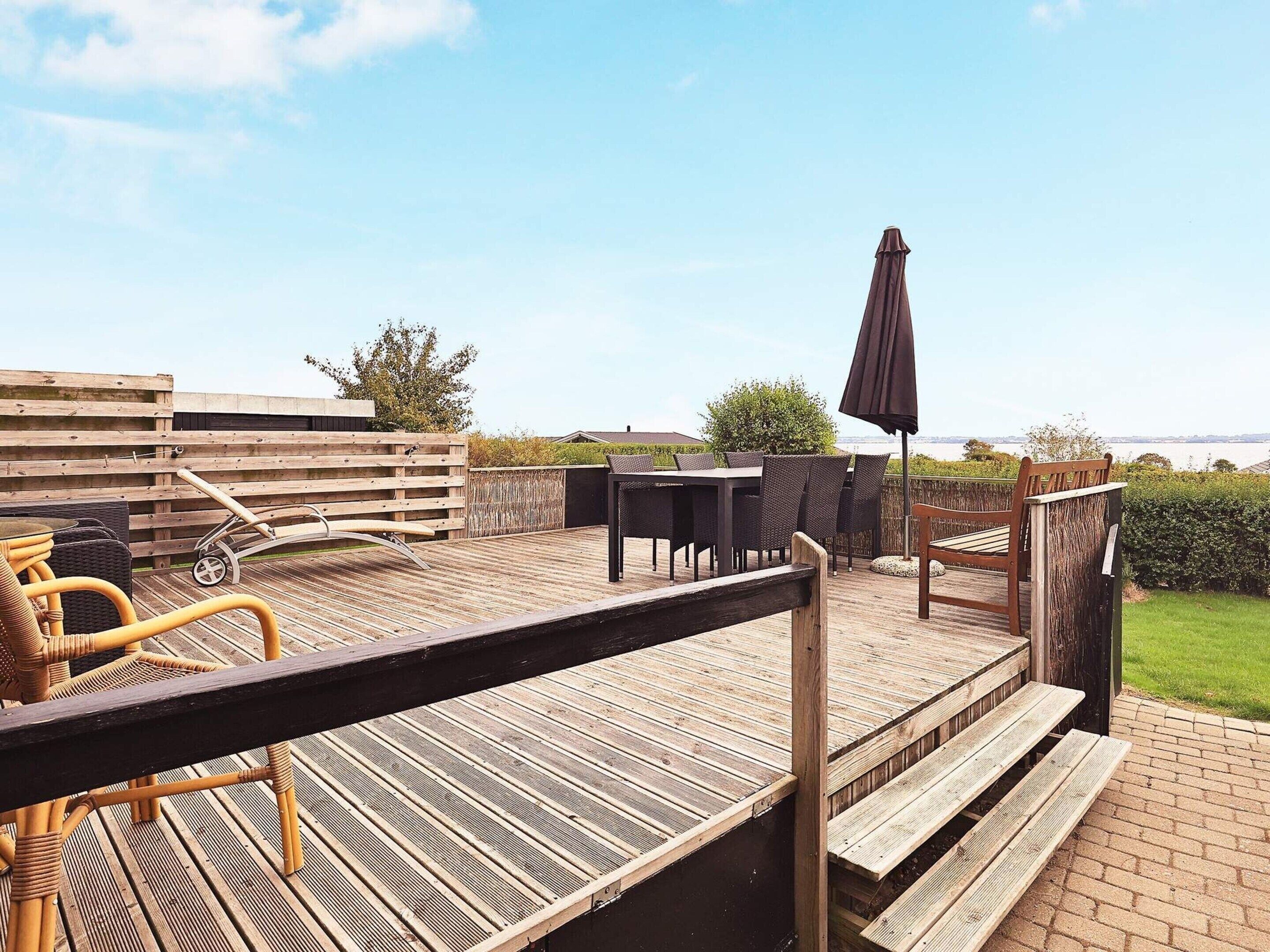 Une terrasse en bois, aménagée avec du mobilier d’extérieur, notamment une table et des chaises, et offrant une vue sur la mer.
