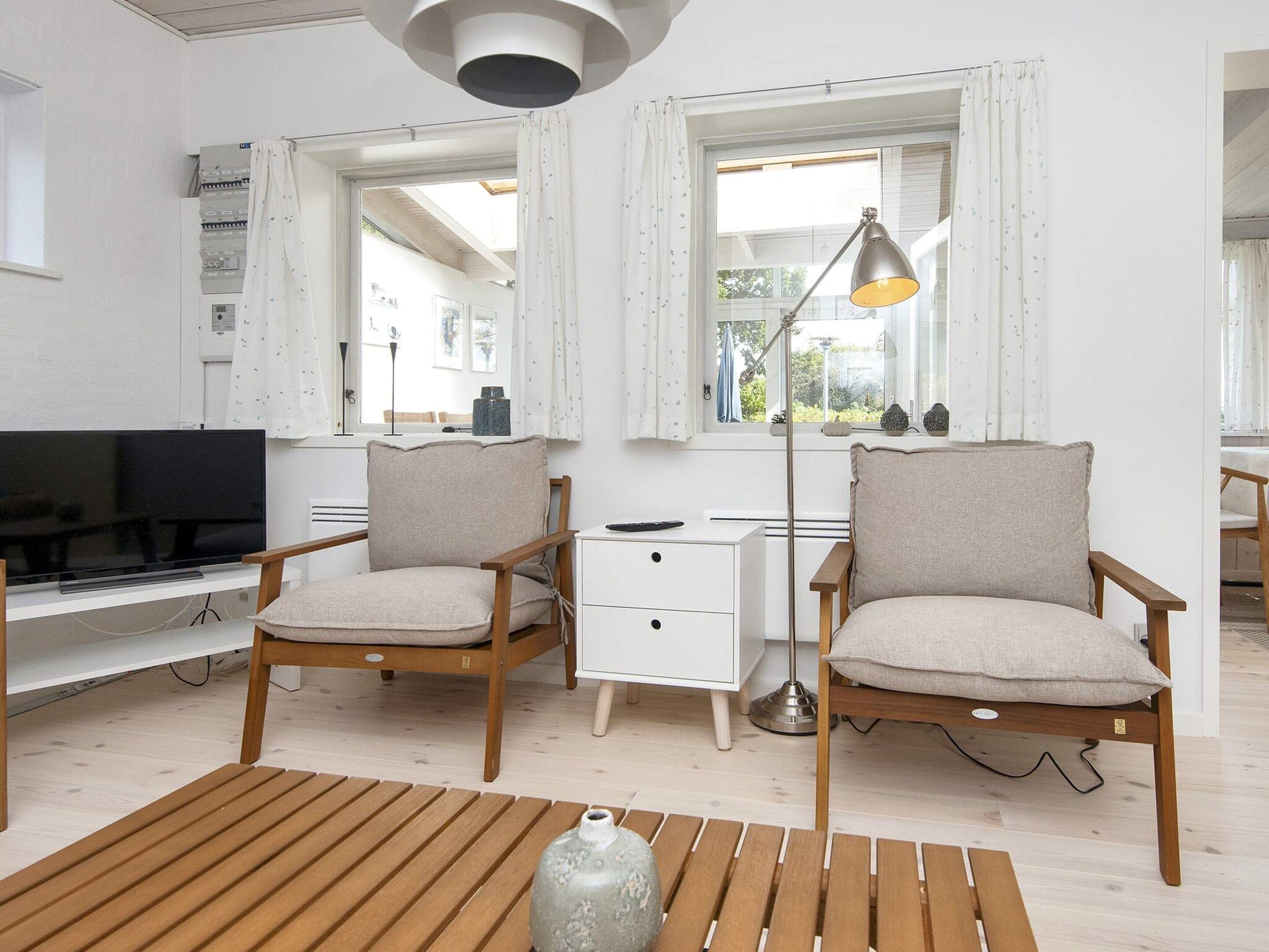 Un salon moderne comprenant un téléviseur, deux fauteuils, un bureau et une lampe.