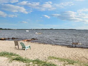 A beach with two chairs, a wooden dock, and calm water with boats. - 6 Person Holiday Home in Sjolund (Sjølund)