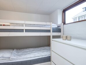 Ein Schlafraum mit Etagenbett, Fenster und Ablagefläche mit zwei Boxen, sowie eine graue Matratze.