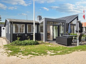 A modern two-story building with a flat roof, large windows, and a dining area with outdoor seating.