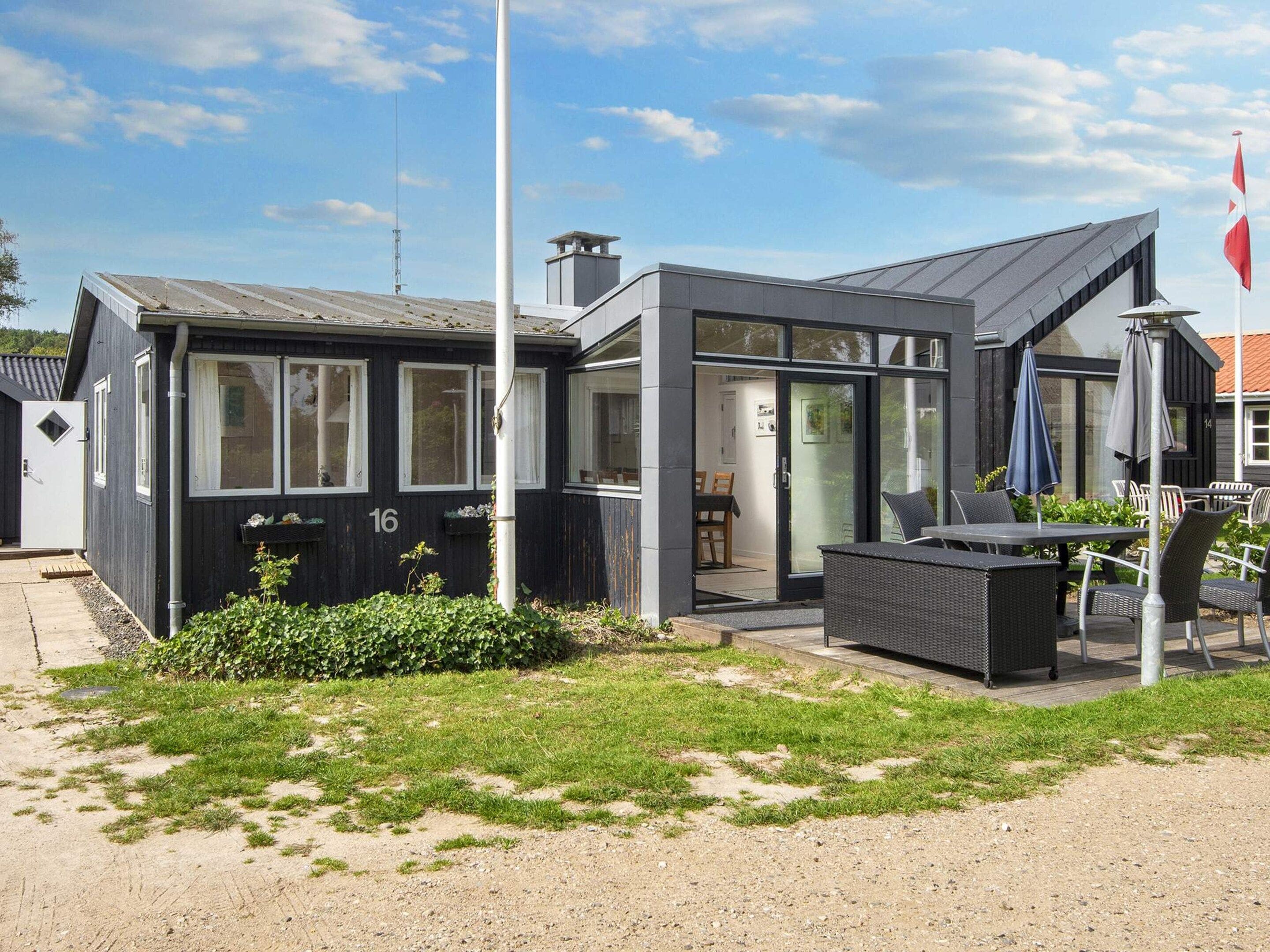 A modern building with a flat roof, large windows, and a patio area with outdoor furniture.
