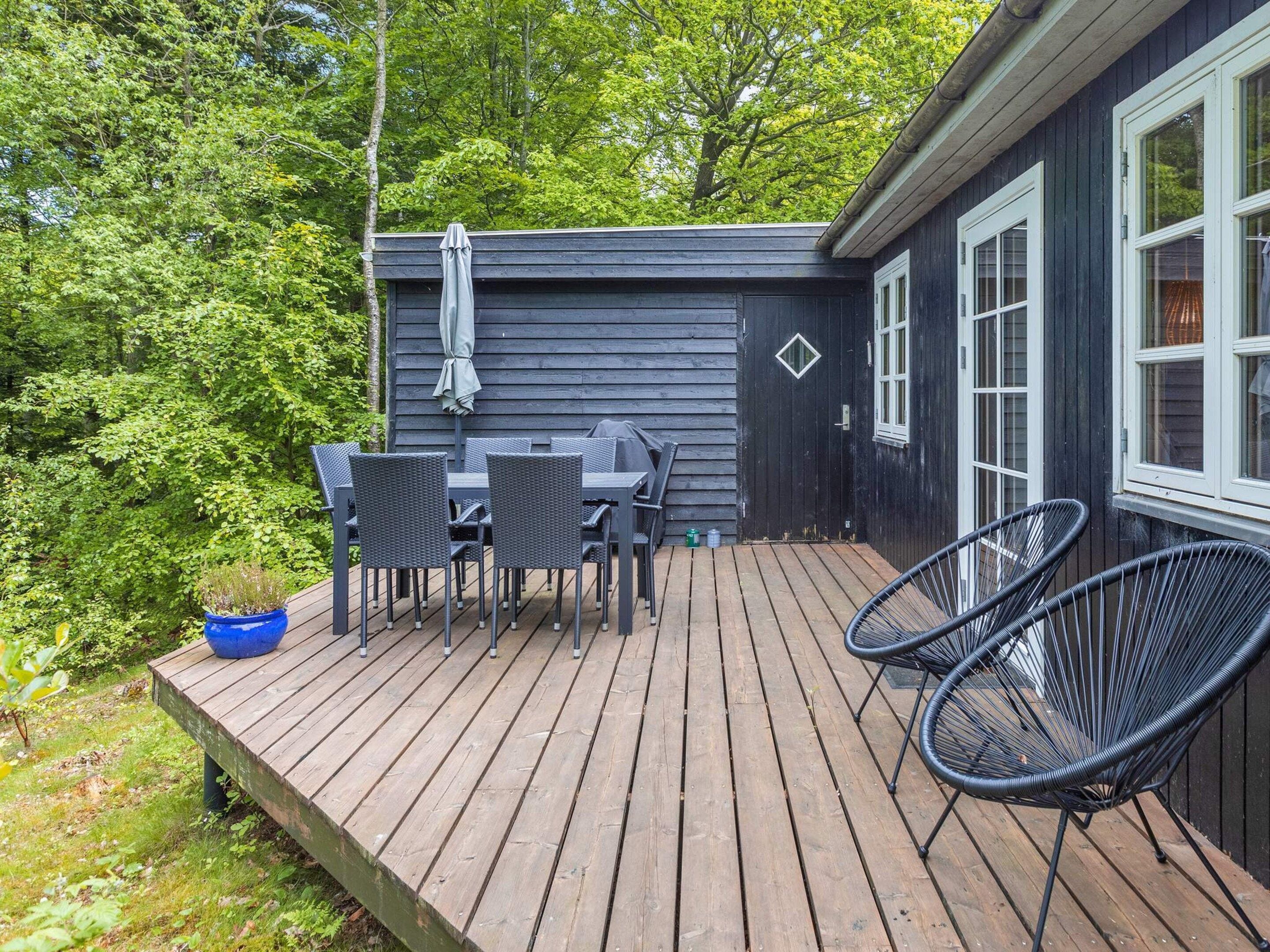 A wooden deck with a table and chairs, a small blue planter, and a black chair.
