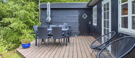 A wooden deck with a table and chairs, a small blue planter, and a black chair.