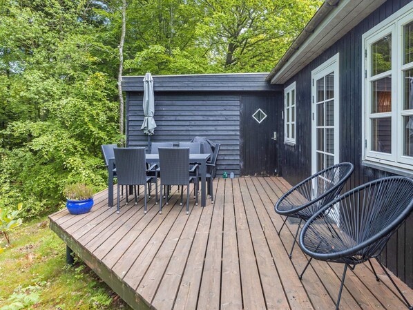 A wooden deck with a table and chairs, a small blue planter, and a black chair.