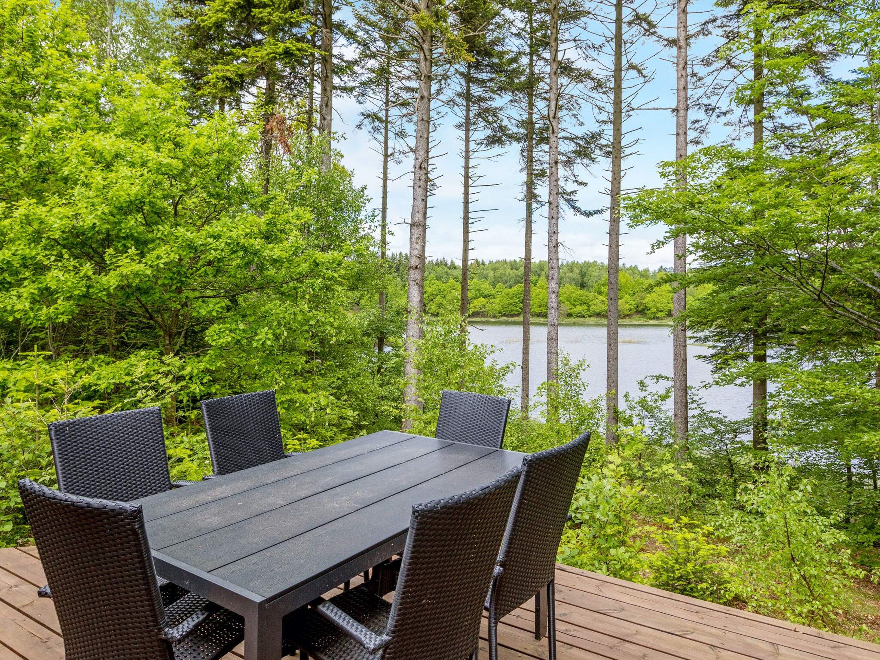 A deck with a table and chairs overlooking a lake, surrounded by dense greenery.