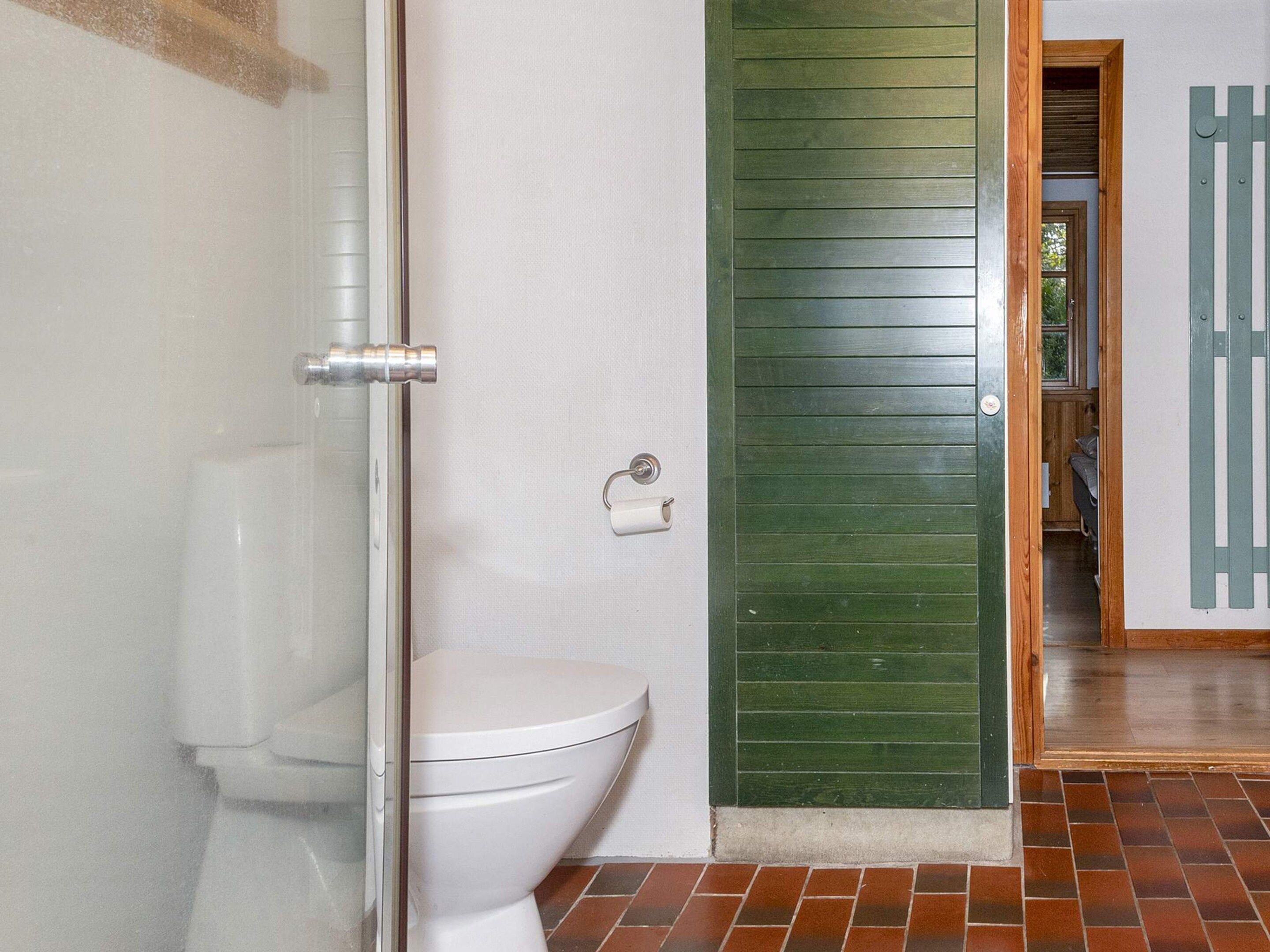 Une salle de bain avec des toilettes blanches, une cabine de douche en verre et une porte verte.