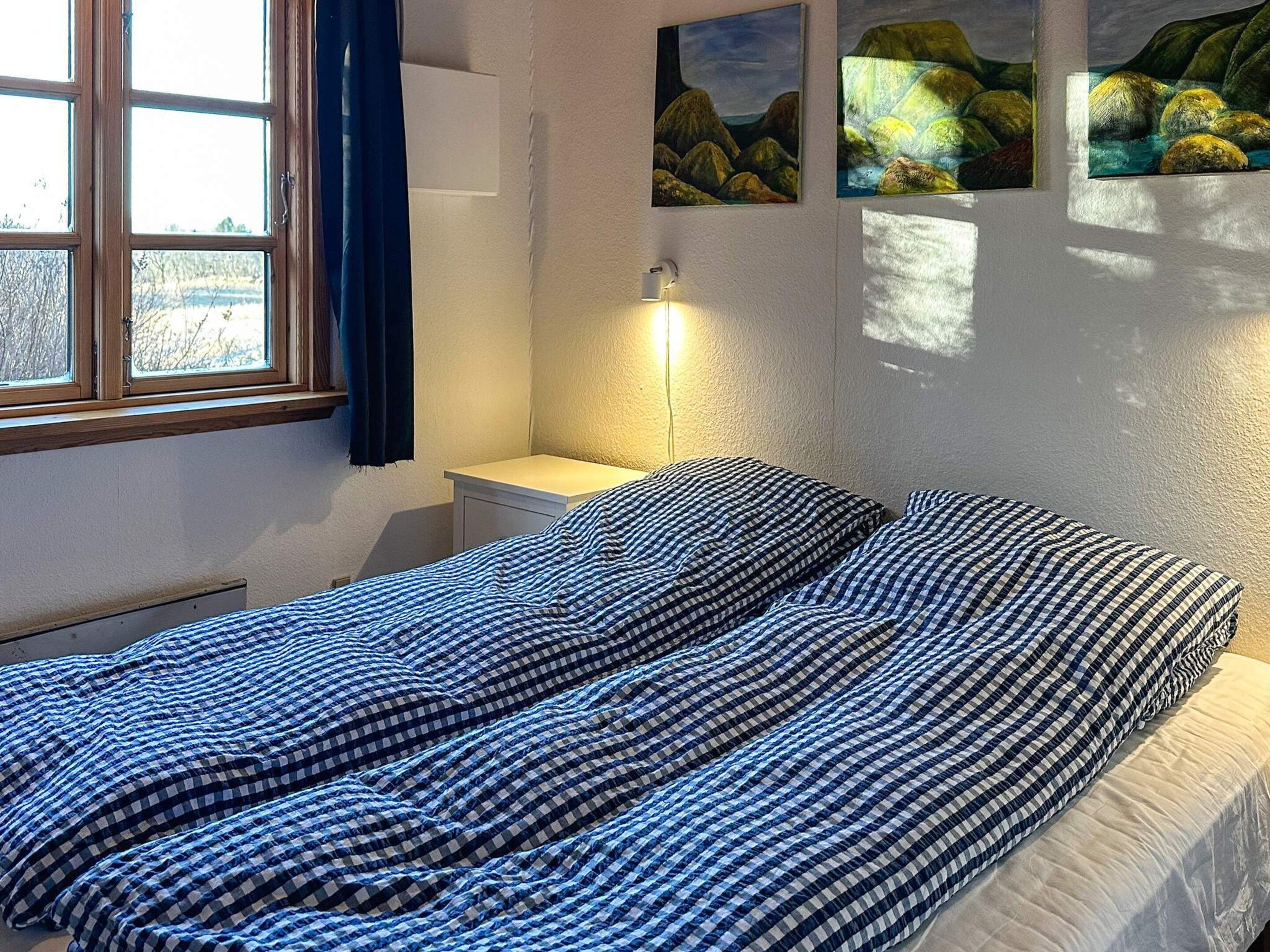 Une chambre à coucher avec un lit, une table de chevet, une lampe et une fenêtre avec des rideaux.