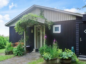 A dark wooden house with a covered porch, a small window, and potted plants in the front yard. - 4 Person Holiday Home in Aars (Aars)