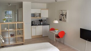 Ein modernes Hotelzimmer mit einem Bett, einem Schreibtisch mit Stuhl, einer kleinen Küchenzeile und einem Fernseher.
