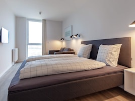 Un dormitorio moderno con una cama grande, una mesita de noche, una lámpara de pared y cortinas en la ventana.