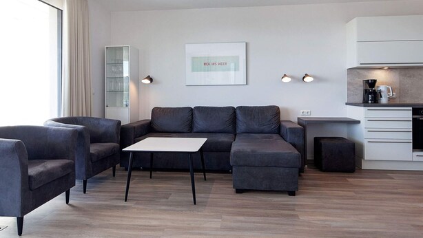 A modern living room with a sectional sofa, a small table, and a coffee machine.