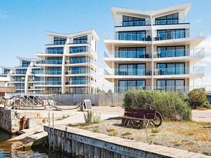 A modern multi-story building with balconies and large windows, located near a dock with a wooden walkway.