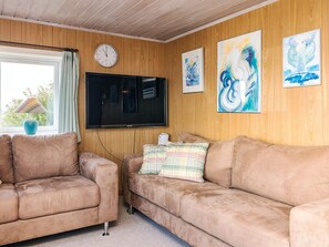A cozy living room with two beige sofas, a flat-screen TV, wooden panel walls, and three abstract paintings. - 4 Person Holiday Home in Farso (Farso)