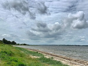 A beach with a grassy foreground and a body of water extending to the horizon under a cloudy sky. - 4 Person Holiday Home in Farso (Farso)