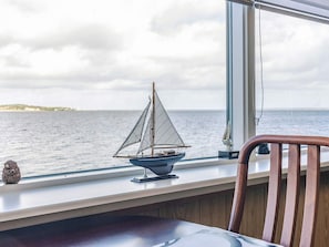 A model sailboat on a windowsill with a view of the sea and a distant shoreline. - 4 Person Holiday Home in Farso (Farso)