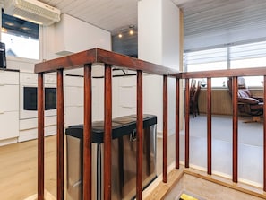 A kitchen with white cabinets, a stainless steel trash can, and a wooden railing.