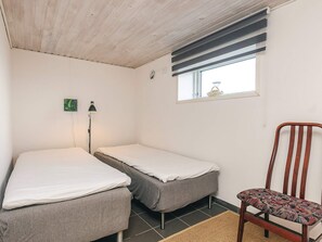 A small, simple room with two single beds, a chair, a lamp, and a window with a view. - 4 Person Holiday Home in Farso (Farso)