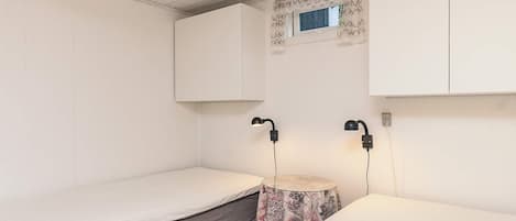 A small, minimalist room with two single beds, a small round table, and a window with a decorative frame.