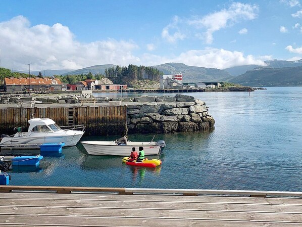 A harbor with boats docked, a lighthouse, and a rocky shoreline.