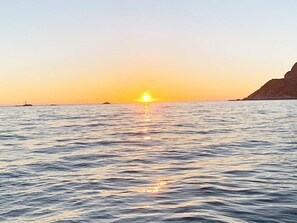 A sunset over calm sea waters with distant landforms.