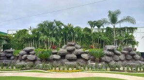 A landscaped area with a rock formation, palm trees, and a pathway. - Family house bridges, long end (Tulum)